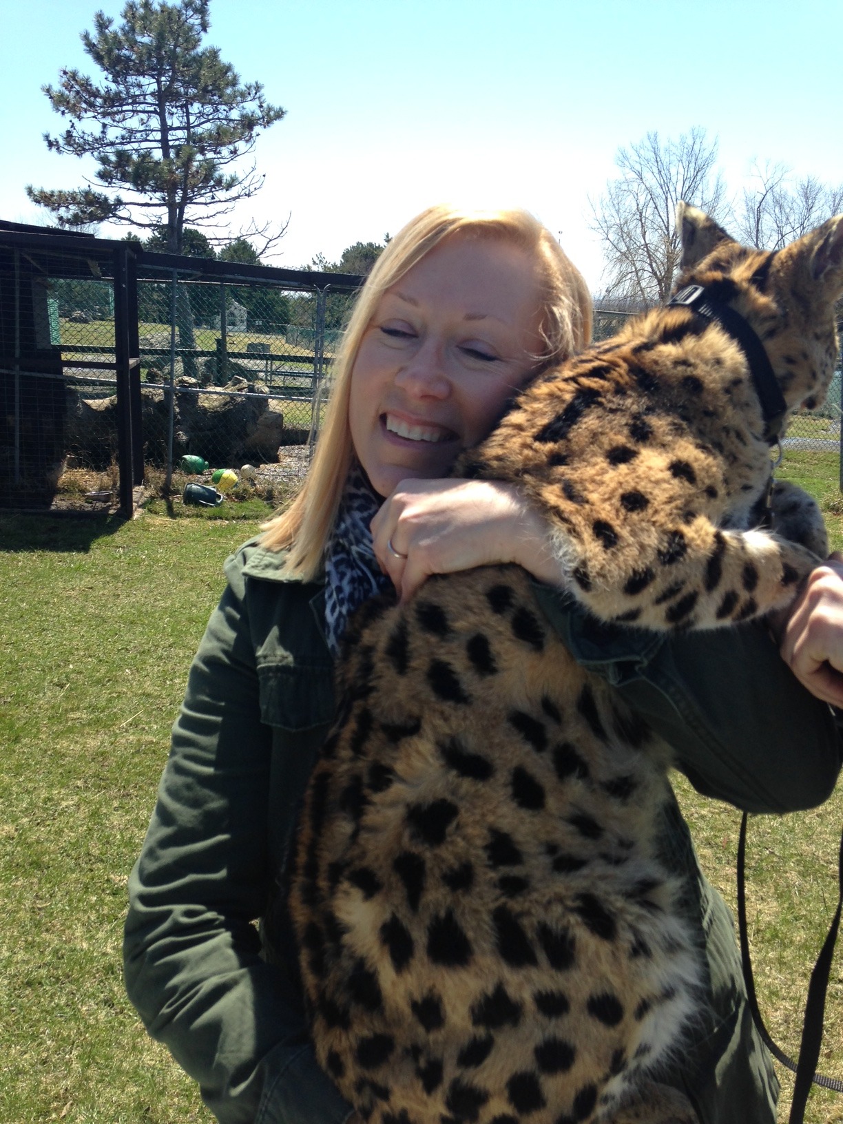 Cat Aulakh smiling while hugging a serval, a spotted wild cat, outdoors on grass